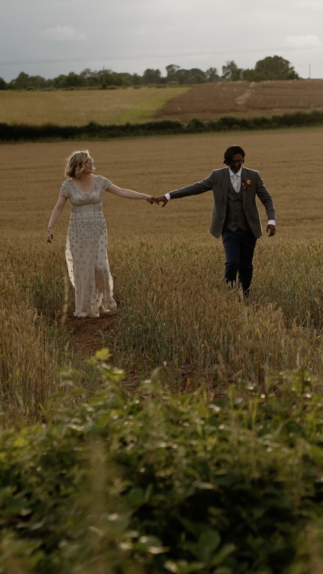 Bride and groom walking in field near Grangefields